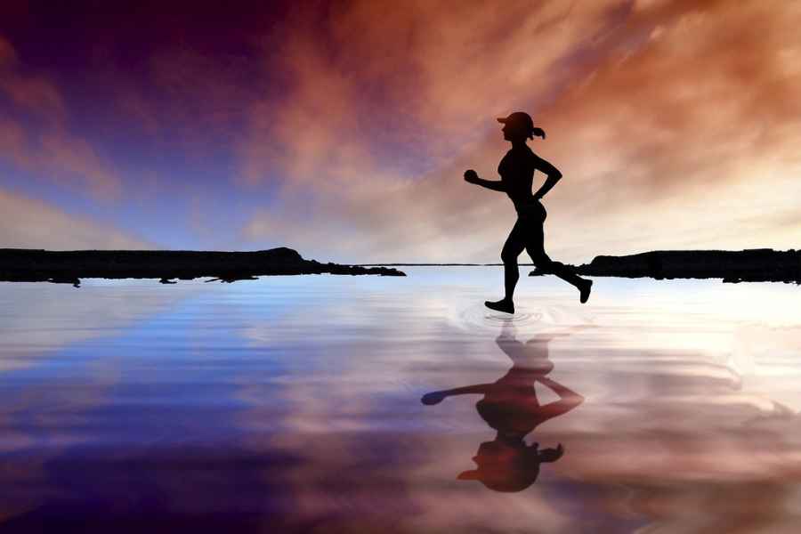 A silhouette of a woman jogging on a beach during sunset